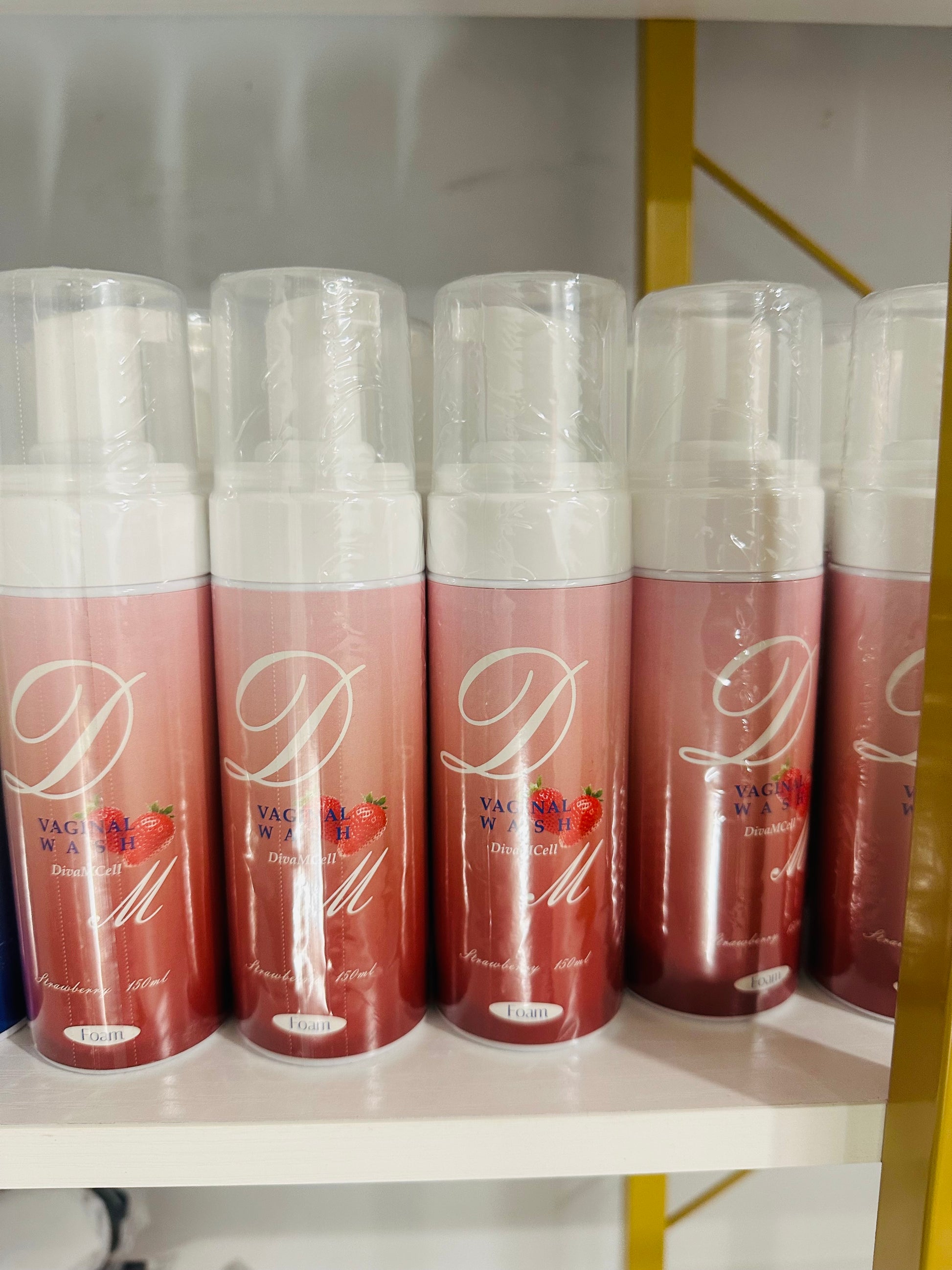 Bottles of strawberry-scented feminine wash with pink and white packaging, arranged in a line on a shelf.